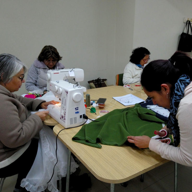 mujeres sobre una mesa de madera con maquinas de cocer participando en la capacitación textil